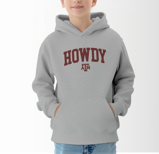 A model wears the Sport Grey Youth Unisex Texas A&M Howdy Varsity Hooded Sweatshirt.  The ﻿Texas A&M Howdy Varsity﻿ graphic is in bold Maroon in a Collegiate style.