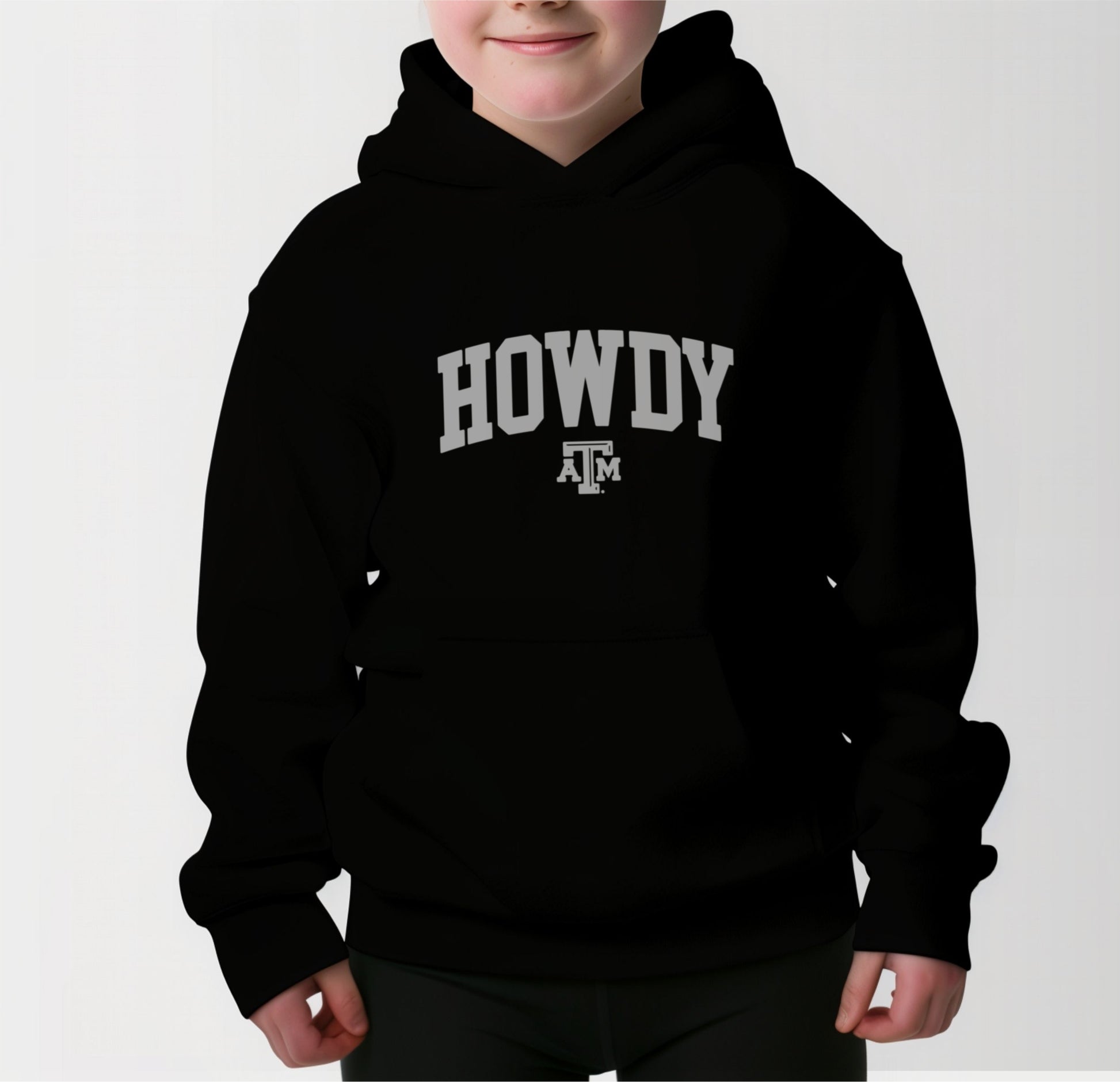 A model wears the Black Youth Unisex Texas A&M Howdy Varsity Hooded Sweatshirt.  The ﻿Texas A&M Howdy Varsity﻿ graphic is in bold White in a Collegiate style.