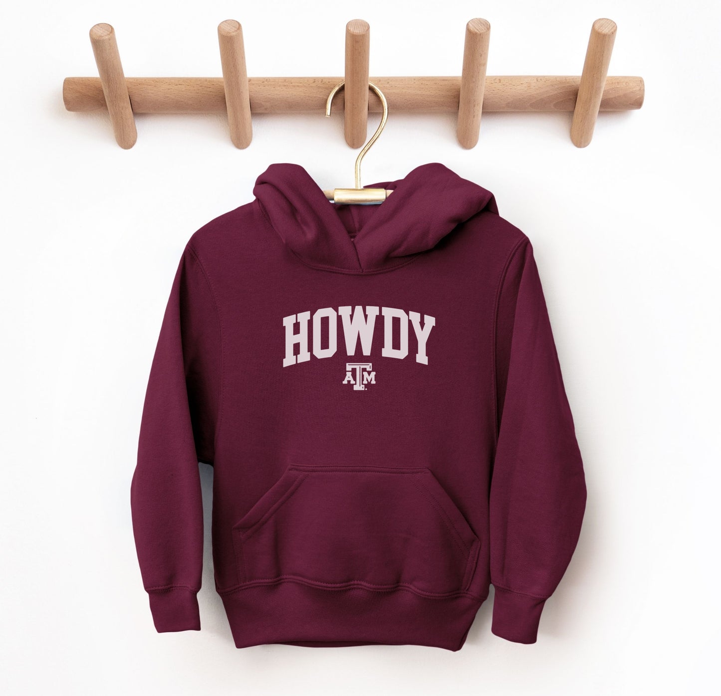 The Maroon Youth Unisex Texas A&M Howdy Varsity Hooded Sweatshirt lays flat on a white background. The ﻿Texas A&M Howdy Varsity﻿ graphic is in bold White in a Collegiate style.