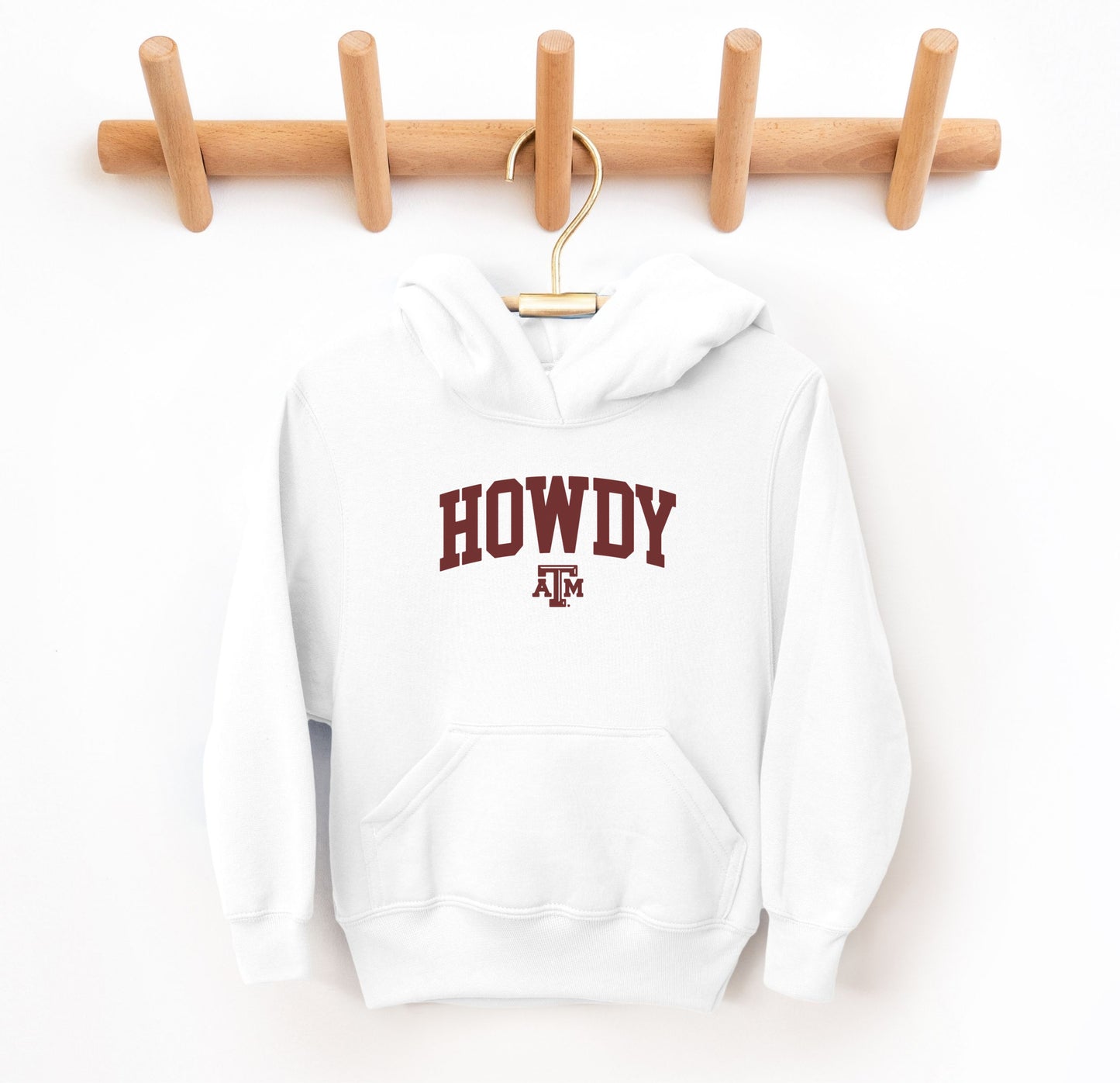 The White Youth Unisex Texas A&M Howdy Varsity Hooded Sweatshirt lays flat on a white background. The ﻿Texas A&M Howdy Varsity﻿ graphic is in bold Maroon in a Collegiate style.