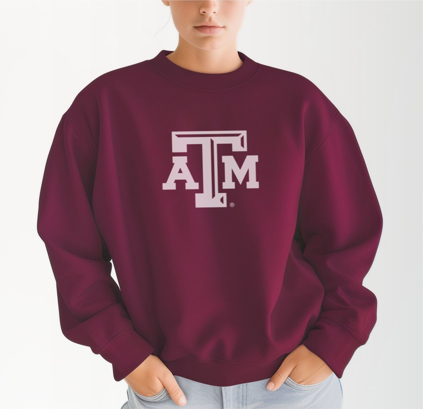 A model wears the Maroon Adult Unisex Texas A&M Logo Crewneck Sweatshirt.  The ﻿Texas A&M Logo﻿ graphic is in bold White in a Varsity style.