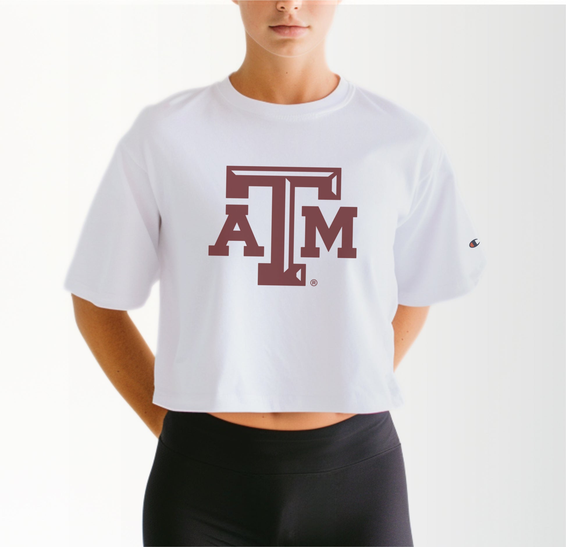 A model wears the White Adult Womens Texas A&M Logo Crop Top.  The ﻿Texas A&M Logo﻿ graphic is in bold Maroon in a Varsity style.