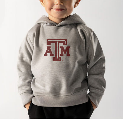 A model wears the Heather Grey Toddler Unisex Texas A&M Logo Hooded Sweatshirt.  The ﻿Texas A&M Logo﻿ graphic is in bold Maroon in a Varsity style.