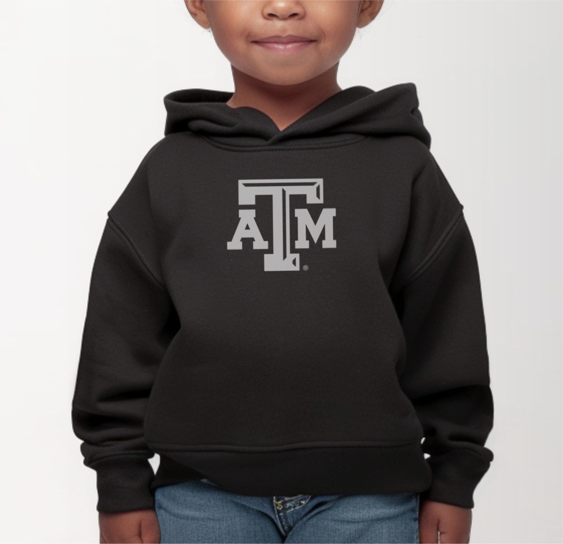 A model wears the Black Toddler Unisex Texas A&M Logo Hooded Sweatshirt.  The ﻿Texas A&M Logo﻿ graphic is in bold White in a Varsity style.