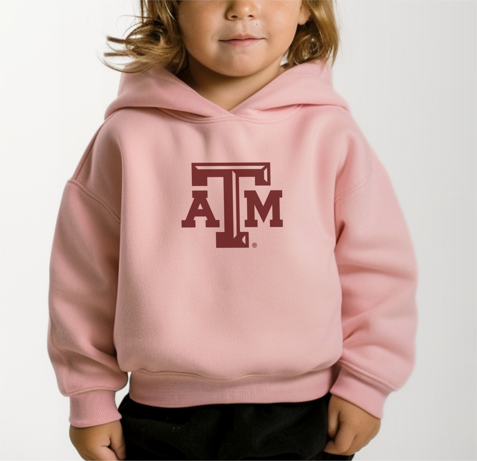 A model wears the Pink Toddler Unisex Texas A&M Logo Hooded Sweatshirt.  The ﻿Texas A&M Logo﻿ graphic is in bold White in a Varsity style.