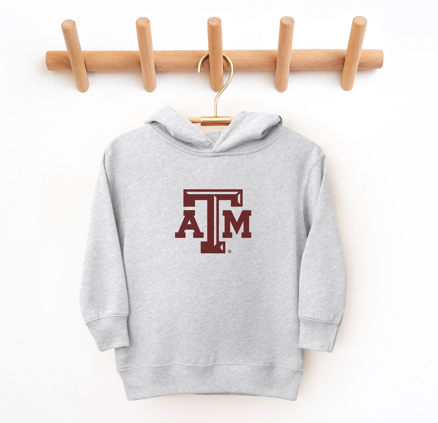 The Heather Grey Toddler Unisex Texas A&M Logo Hooded Sweatshirt lays flat on a white background. The ﻿Texas A&M Logo﻿ graphic is in bold Maroon in a Varsity style.