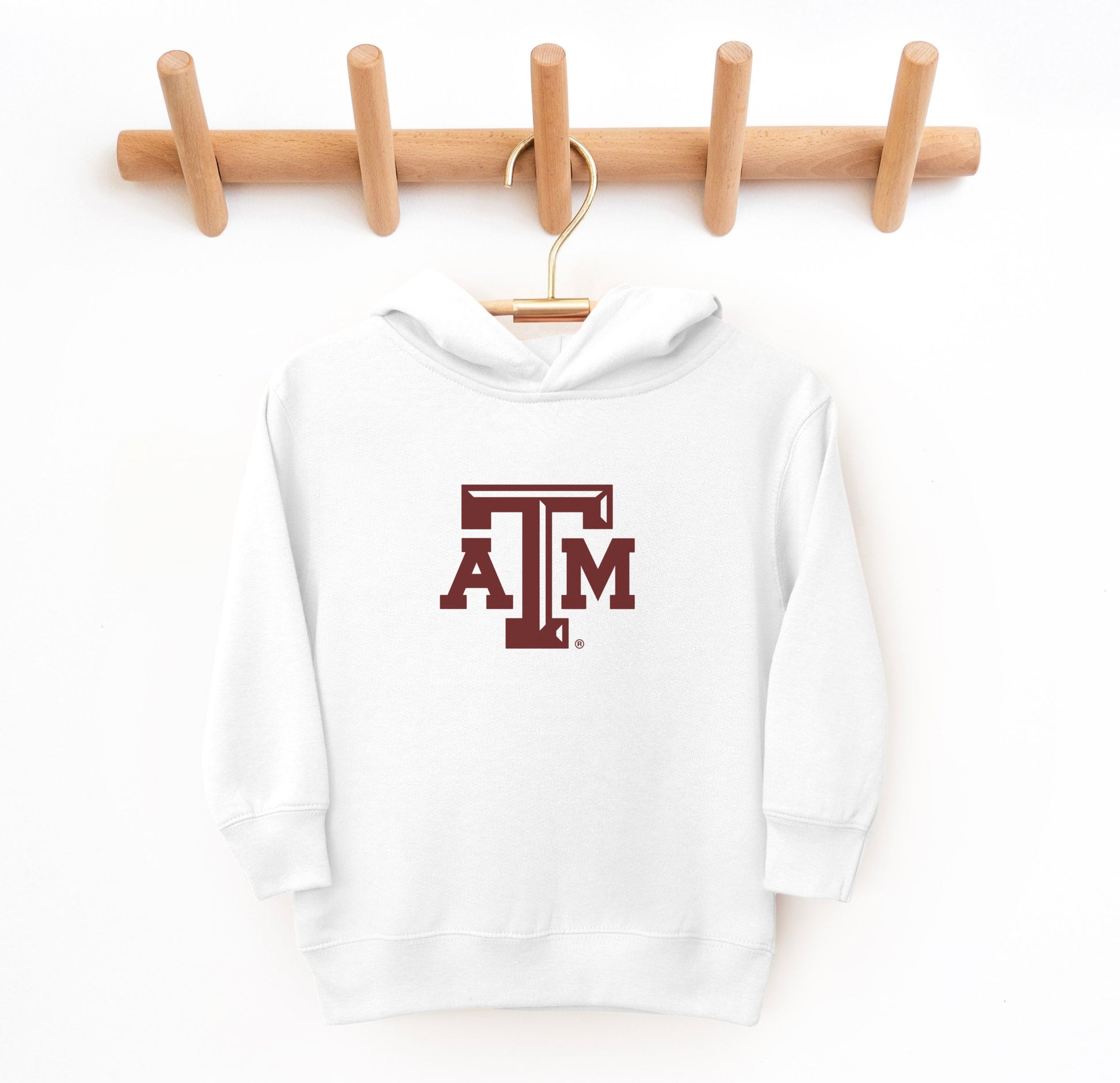 The White Toddler Unisex Texas A&M Logo Hooded Sweatshirt lays flat on a white background. The ﻿Texas A&M Logo﻿ graphic is in bold Maroon in a Varsity style.