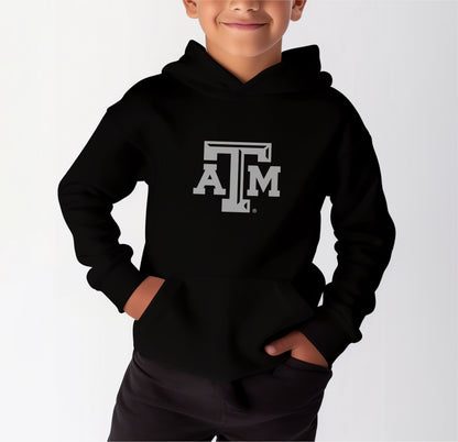 A model wears the Black Youth Unisex Texas A&M Logo Hooded Sweatshirt.  The ﻿Texas A&M Logo﻿ graphic is in bold White in a Varsity style.