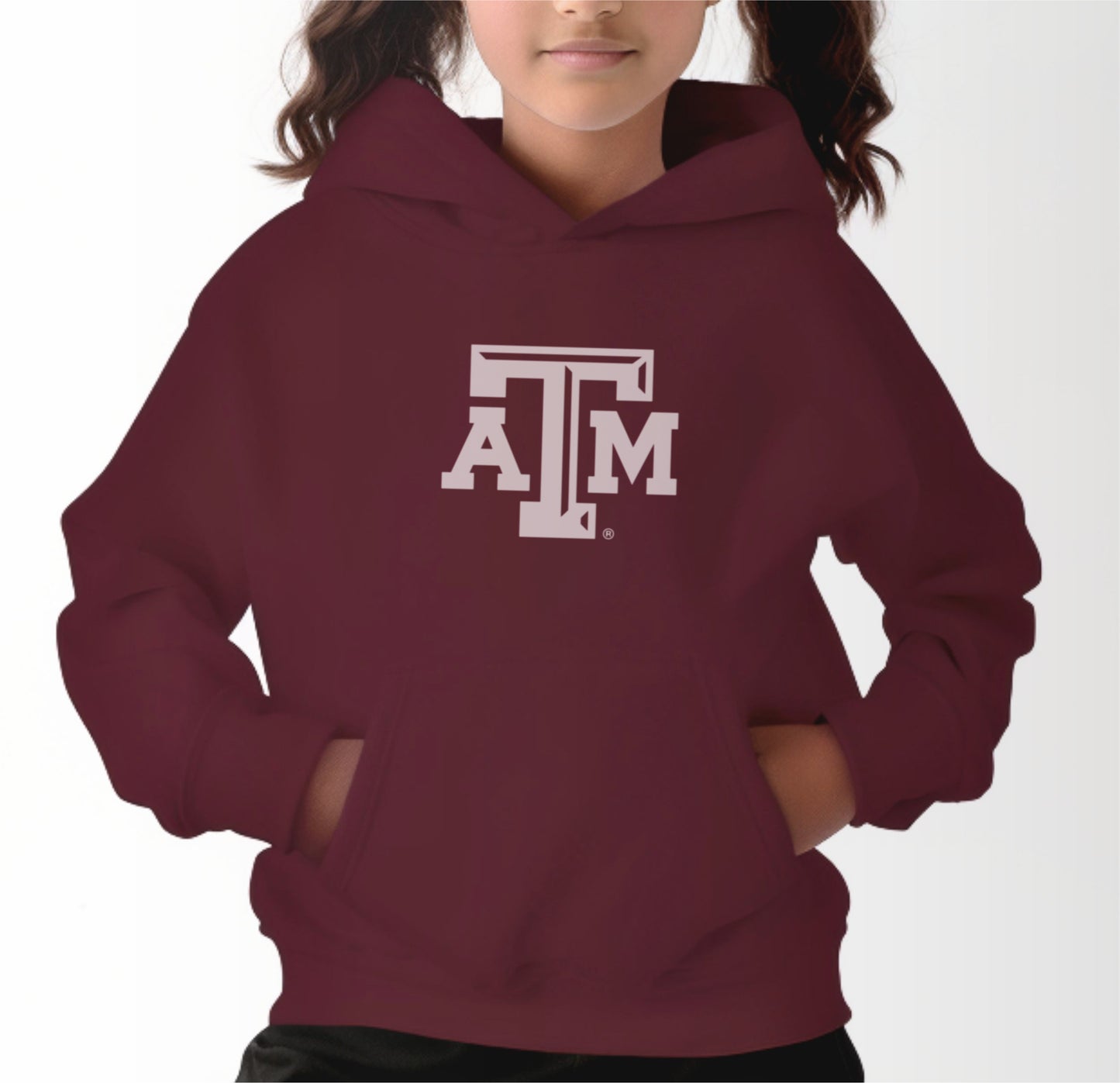 A model wears the Maroon Youth Unisex Texas A&M Logo Hooded Sweatshirt.  The ﻿Texas A&M Logo﻿ graphic is in bold White in a Varsity style.