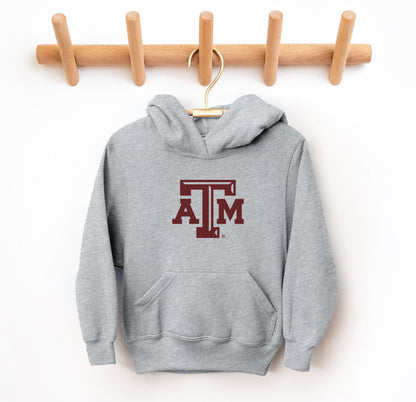 The Sport Grey Youth Unisex Texas A&M Logo Hooded Sweatshirt lays flat on a white background. The ﻿Texas A&M Logo﻿ graphic is in bold Maroon in a Varsity style.