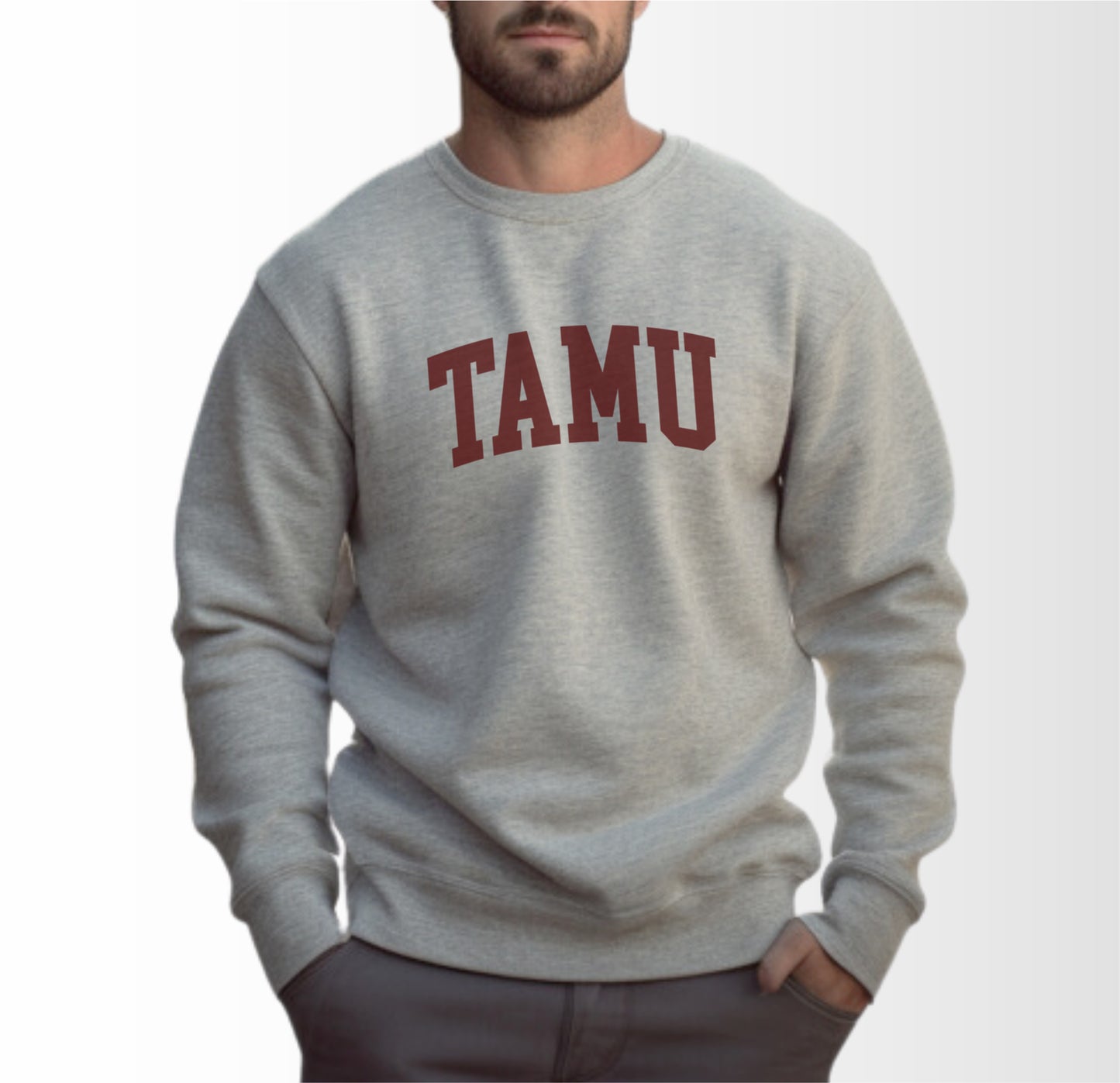 A model wears the Sport Grey Adult Unisex Texas A&M TAMU Crewneck Sweatshirt.  The ﻿Texas A&M TAMU﻿ graphic is in bold Maroon in a Collegiate style.