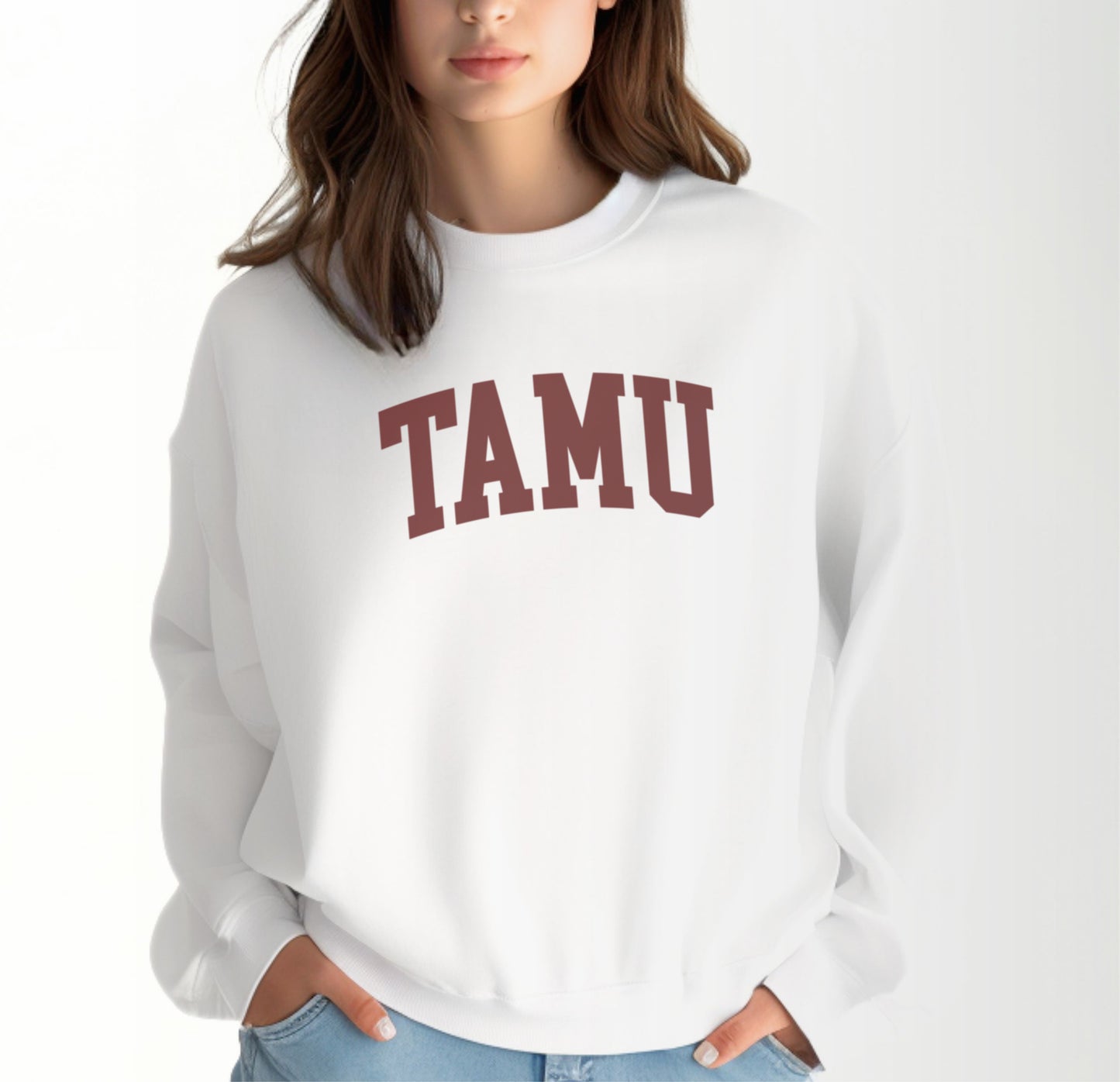 A model wears the White Adult Unisex Texas A&M TAMU Crewneck Sweatshirt.  The ﻿Texas A&M TAMU﻿ graphic is in bold Maroon in a Collegiate style.