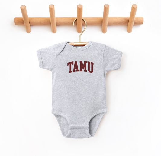 The Heather Grey Infant Unisex Texas A&M TAMU Bodysuit lays flat on a white background. The ﻿Texas A&M TAMU﻿ graphic is in bold Maroon in a Collegiate style.