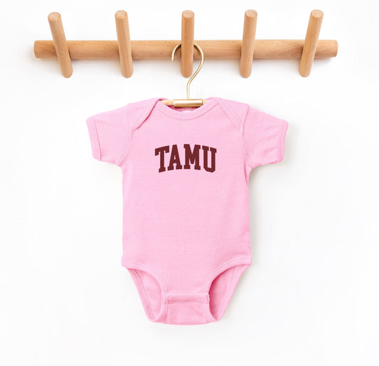 The Pink Infant Unisex Texas A&M TAMU Bodysuit lays flat on a white background. The ﻿Texas A&M TAMU﻿ graphic is in bold Maroon in a Collegiate style.