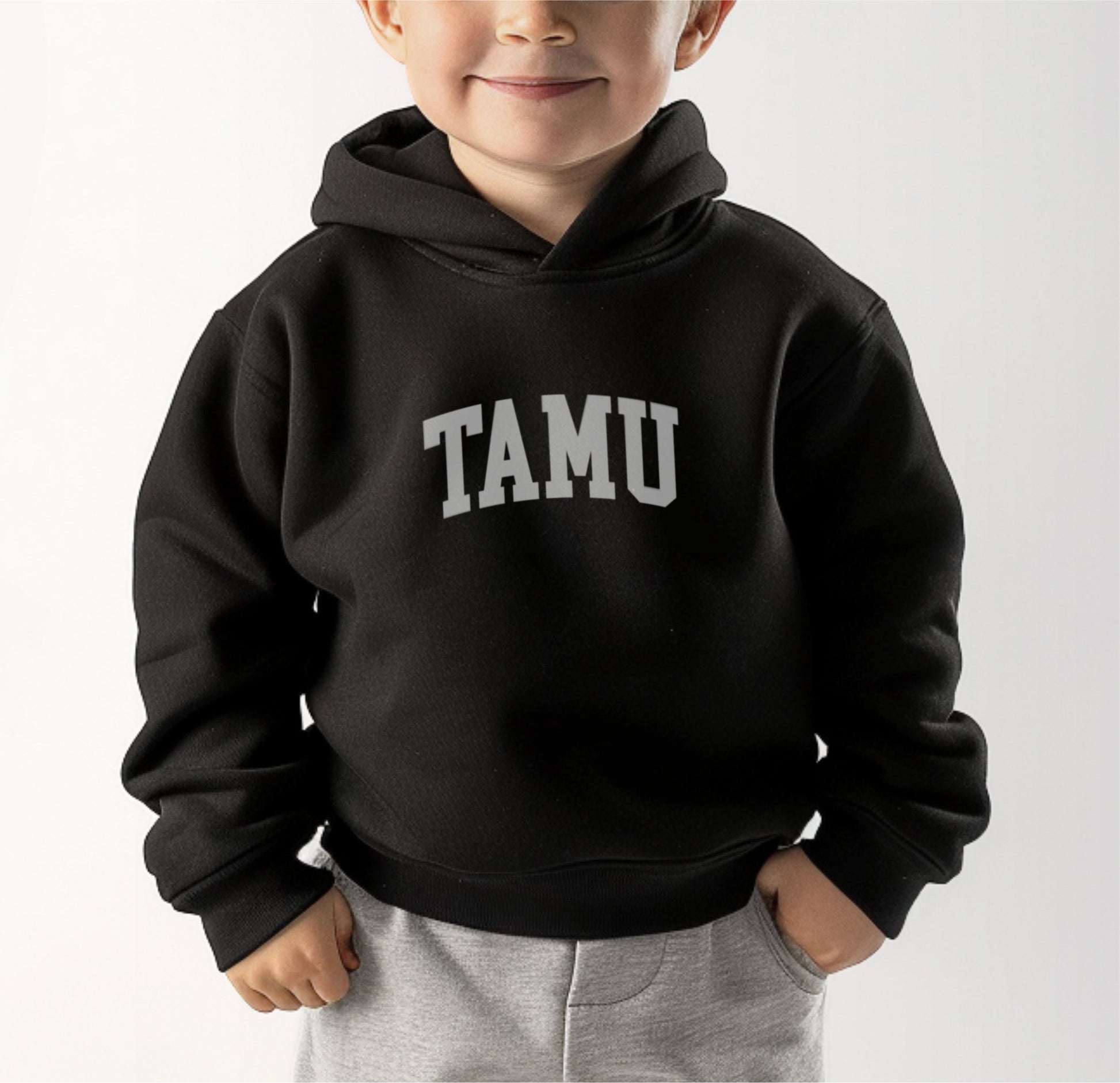 A model wears the Black Toddler Unisex Texas A&M TAMU Hooded Sweatshirt.  The ﻿Texas A&M TAMU﻿ graphic is in bold White in a Collegiate style.