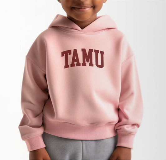 A model wears the Pink Toddler Unisex Texas A&M TAMU Hooded Sweatshirt.  The ﻿Texas A&M TAMU﻿ graphic is in bold White in a Collegiate style.