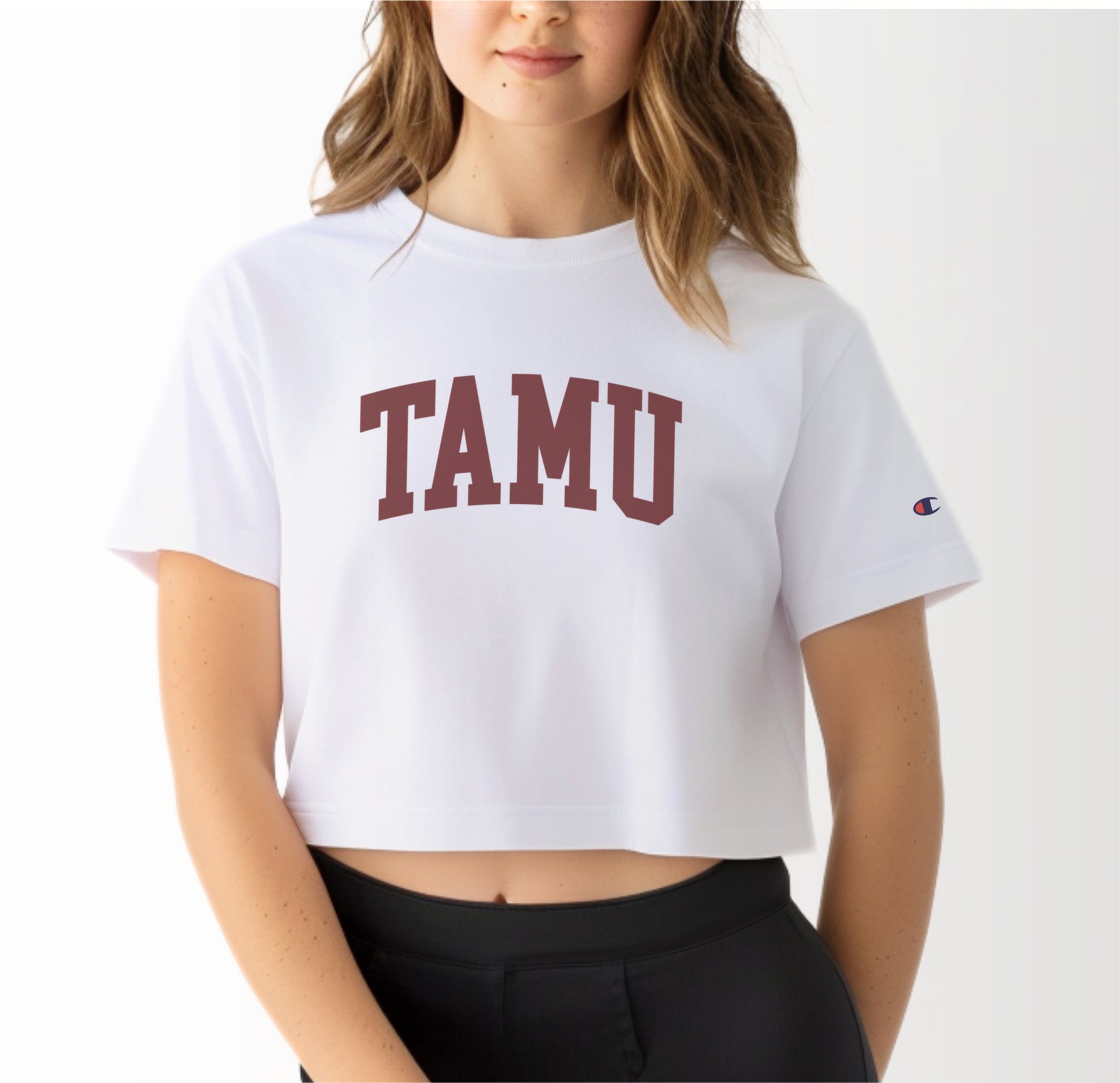 A model wears the White Adult Womens Texas A&M TAMU Crop Top.  The ﻿Texas A&M TAMU﻿ graphic is in bold Maroon in a Collegiate style.