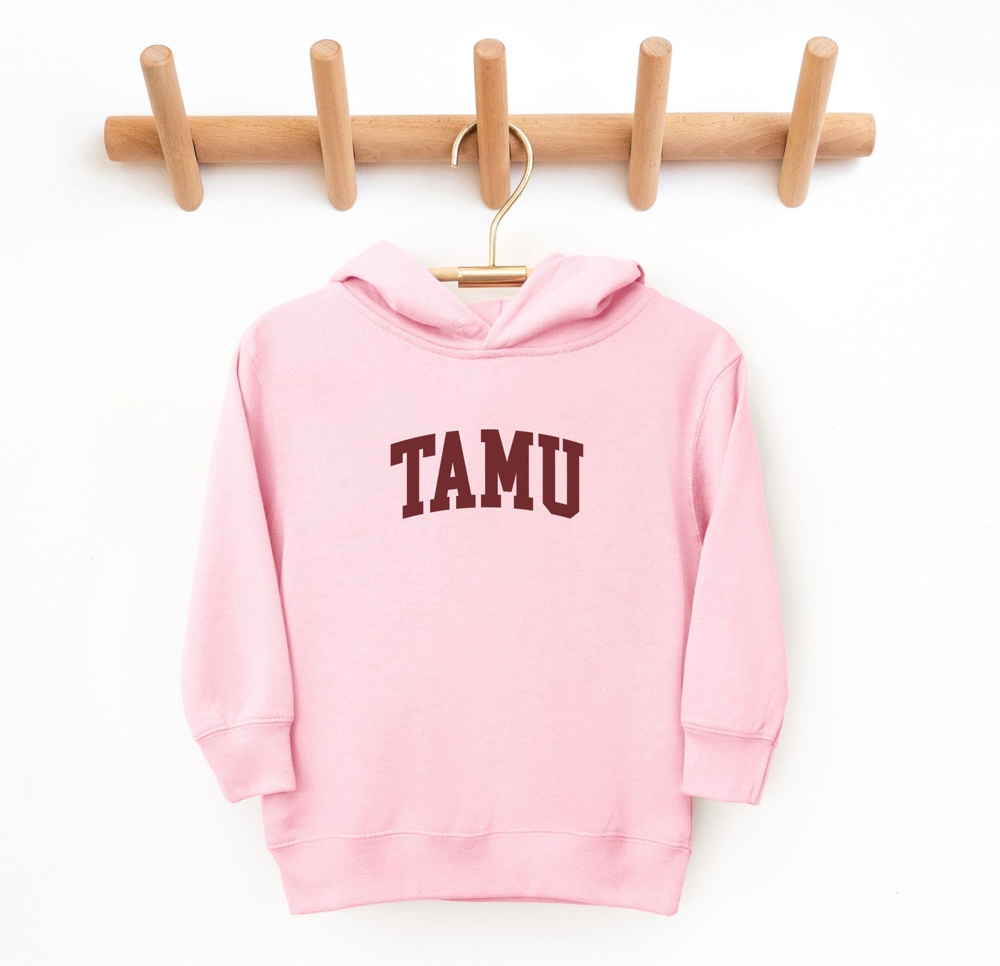 The Pink Toddler Unisex Texas A&M TAMU Hooded Sweatshirt lays flat on a white background. The ﻿Texas A&M TAMU﻿ graphic is in bold White in a Collegiate style.