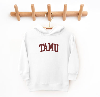 The White Toddler Unisex Texas A&M TAMU Hooded Sweatshirt lays flat on a white background. The ﻿Texas A&M TAMU﻿ graphic is in bold Maroon in a Collegiate style.