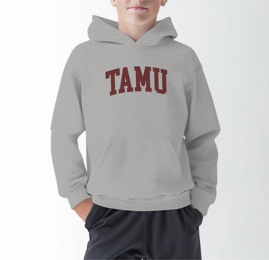 A model wears the Sport Grey Youth Unisex Texas A&M TAMU Hooded Sweatshirt.  The ﻿Texas A&M TAMU﻿ graphic is in bold Maroon in a Collegiate style.