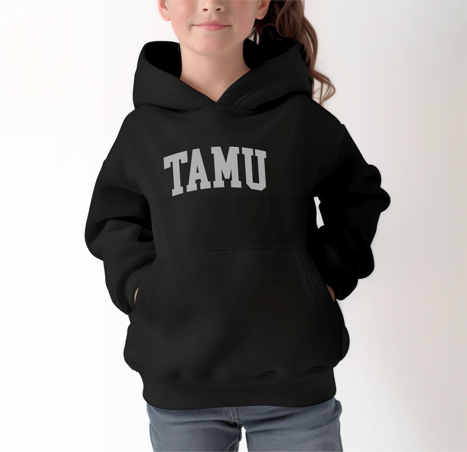 A model wears the Black Youth Unisex Texas A&M TAMU Hooded Sweatshirt.  The ﻿Texas A&M TAMU﻿ graphic is in bold White in a Collegiate style.