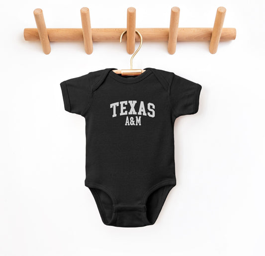 The Black Infant Unisex Texas A&M Varsity Bodysuit lays flat on a white background. The ﻿Texas A&M Varsity﻿ graphic is in bold White in a Collegiate style.