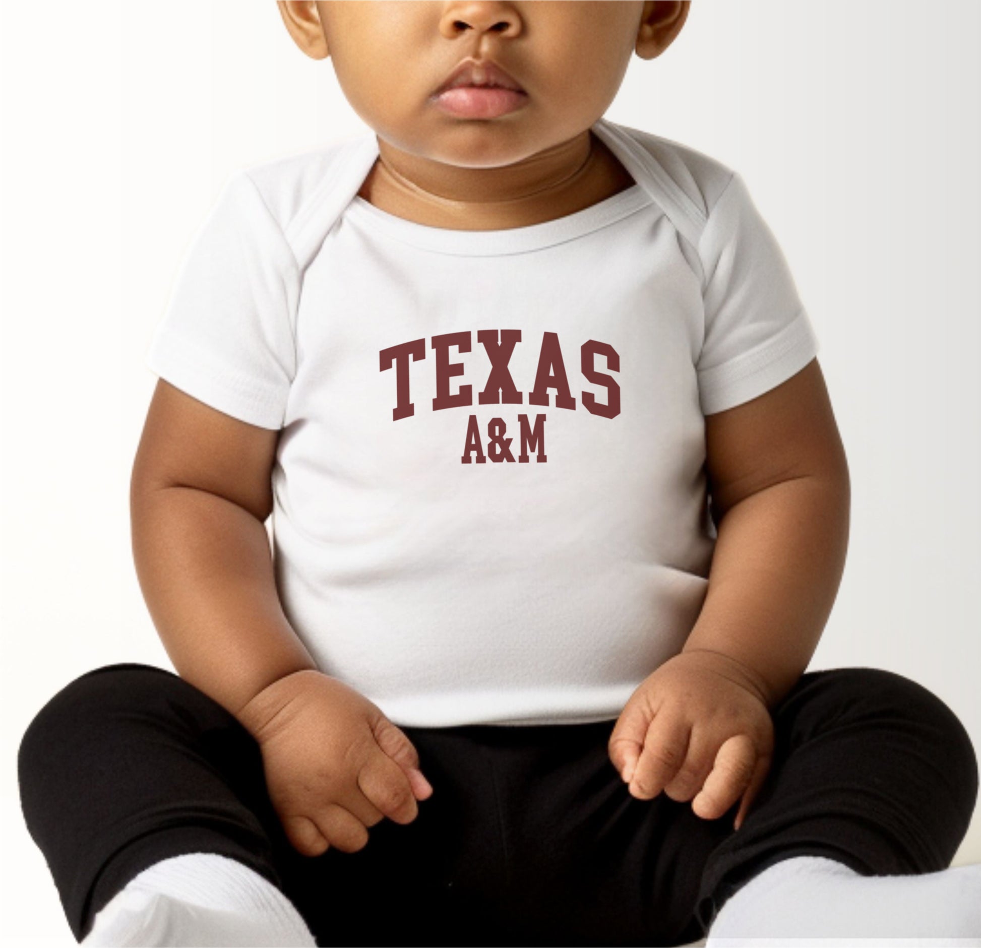 A model wears the Black Infant Unisex Texas A&M Varsity Bodysuit.  The ﻿Texas A&M Varsity﻿ graphic is in bold White in a Collegiate style.