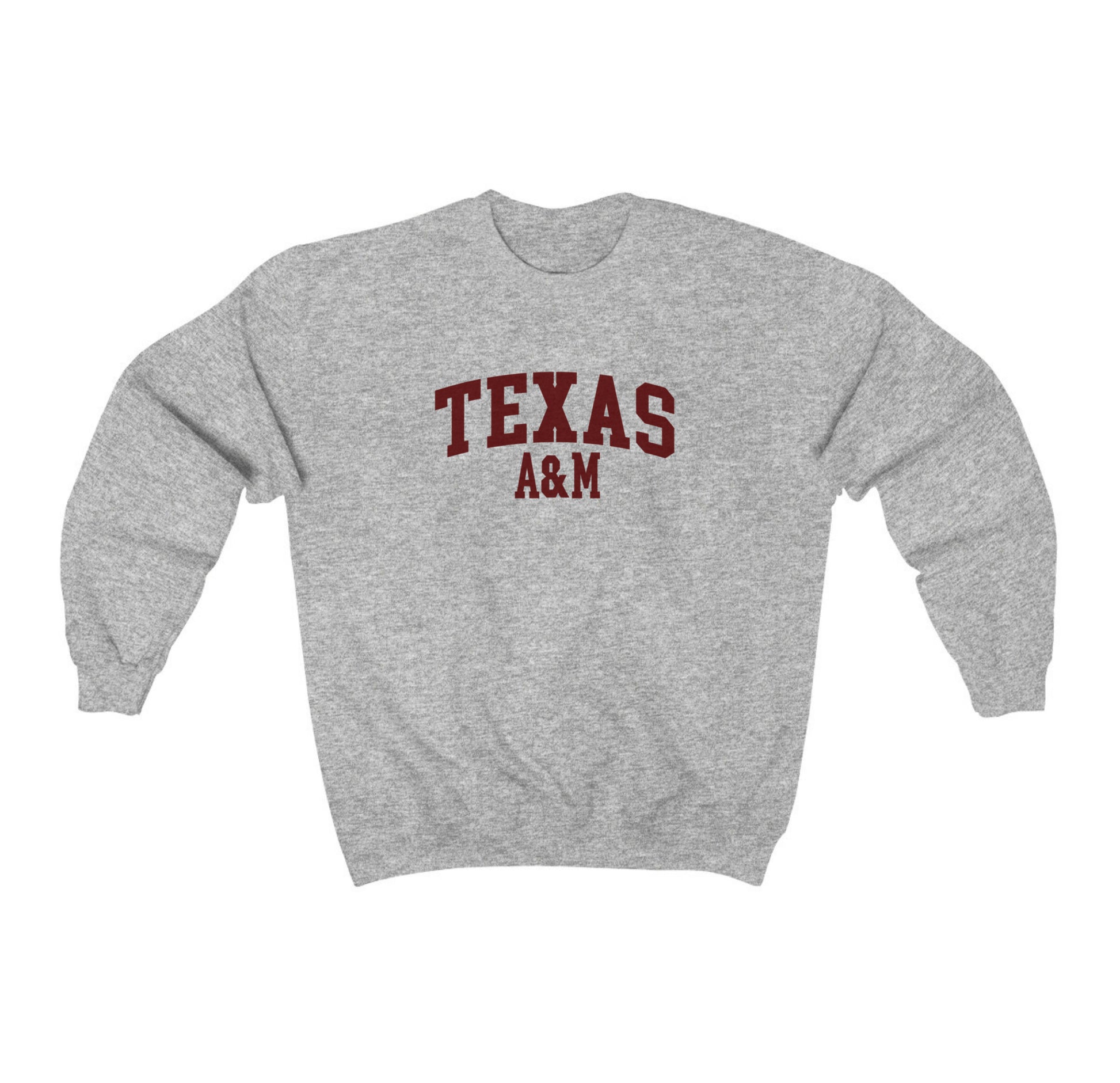 The Sport Grey Adult Unisex Texas A&M Varsity Crewneck Sweatshirt lays flat on a white background. The ﻿Texas A&M Varsity﻿ graphic is in bold Maroon in a Collegiate style.