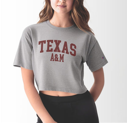 A model wears the Oxford Grey Adult Womens Texas A&M Varsity Crop Top.  The ﻿Texas A&M Varsity﻿ graphic is in bold Maroon in a Collegiate style.