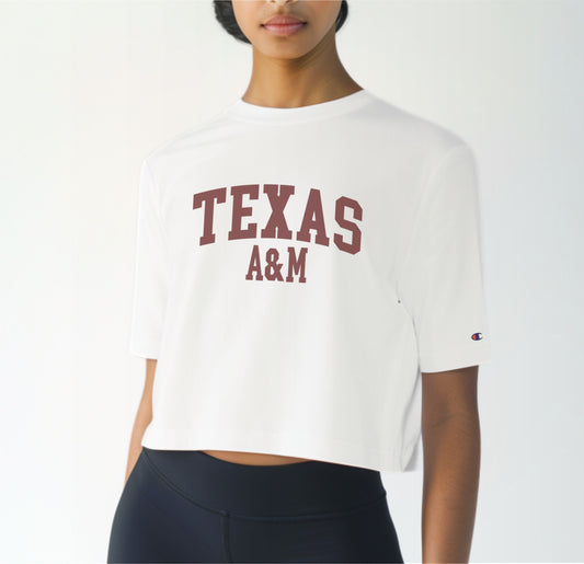 A model wears the White Adult Womens Texas A&M Varsity Crop Top.  The ﻿Texas A&M Varsity﻿ graphic is in bold Maroon in a Collegiate style.