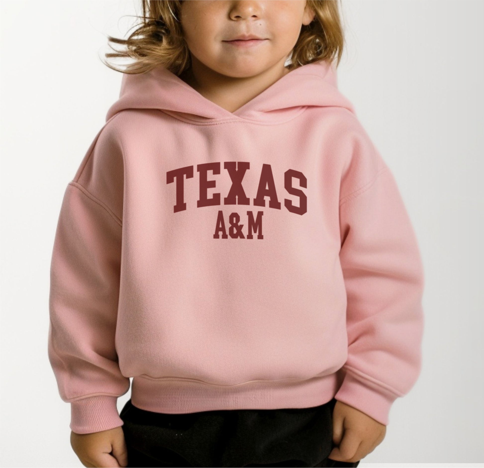 A model wears the Pink Toddler Unisex Texas A&M Varsity Hooded Sweatshirt.  The ﻿Texas A&M Varsity﻿ graphic is in bold White in a Collegiate style.