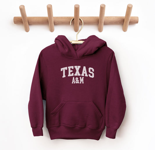 The Maroon Youth Unisex Texas A&M Varsity Hooded Sweatshirt lays flat on a white background. The ﻿Texas A&M Varsity﻿ graphic is in bold White in a Collegiate style.