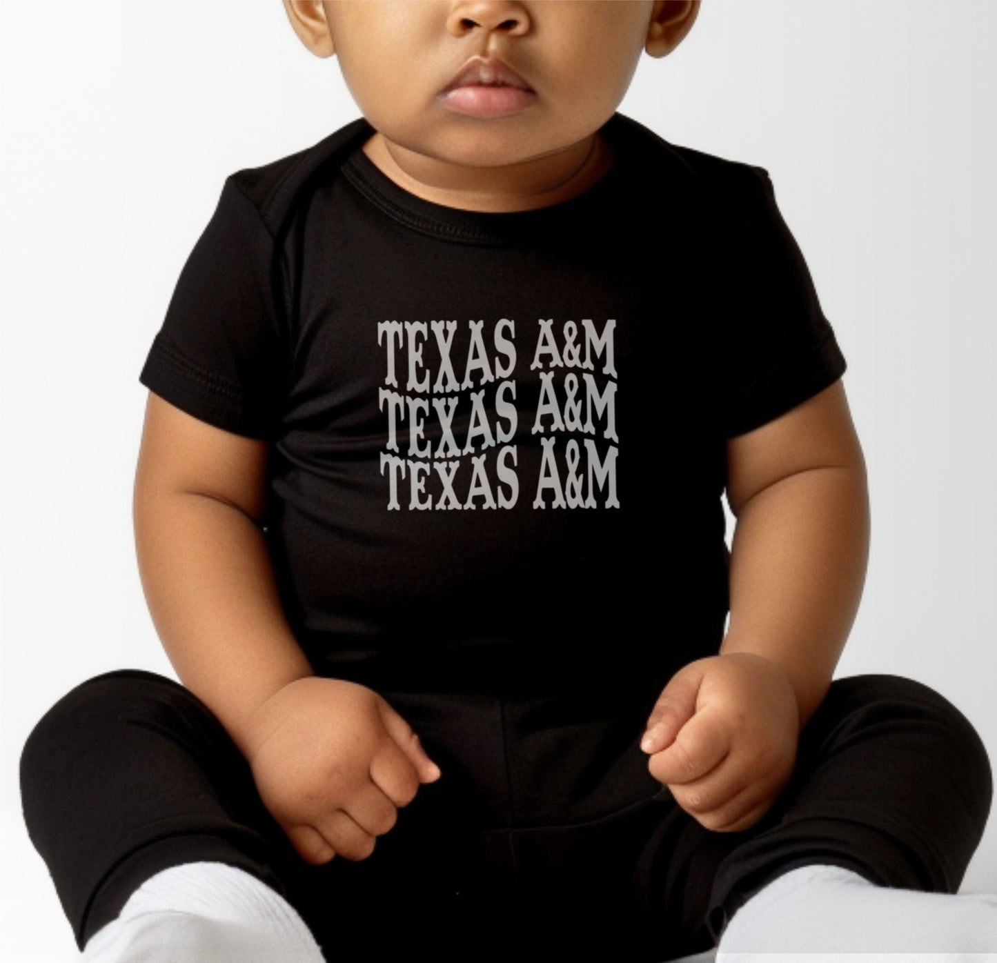 A model wears the Heather Grey Infant Unisex Texas A&M Western Bodysuit.  The ﻿Texas A&M Western﻿ graphic is in bold Maroon in a Western style.