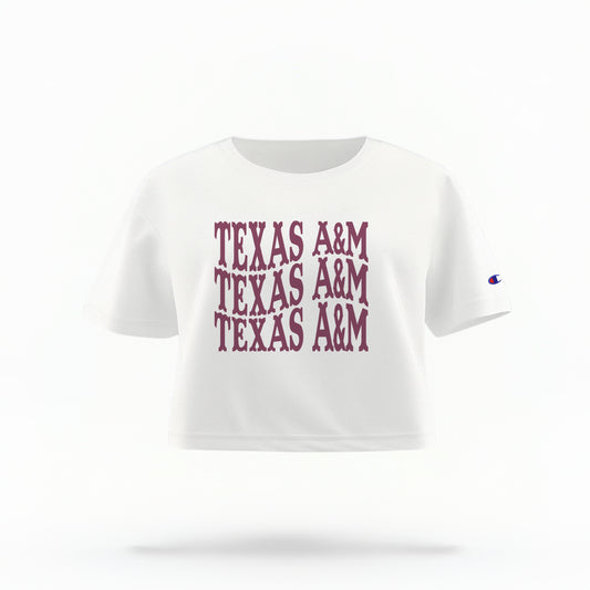 The White Adult Womens Texas A&M Western Crop Top lays flat on a white background. The ﻿Texas A&M Western﻿ graphic is in bold Maroon in a Western style.