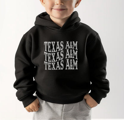 A model wears the Black Toddler Unisex Texas A&M Western Hooded Sweatshirt.  The ﻿Texas A&M Western﻿ graphic is in bold White in a Western style.