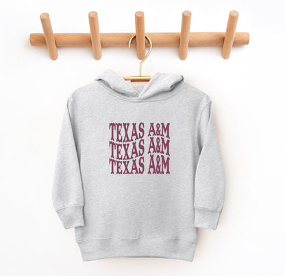 The Heather Grey Toddler Unisex Texas A&M Western Hooded Sweatshirt lays flat on a white background. The ﻿Texas A&M Western﻿ graphic is in bold Maroon in a Western style.