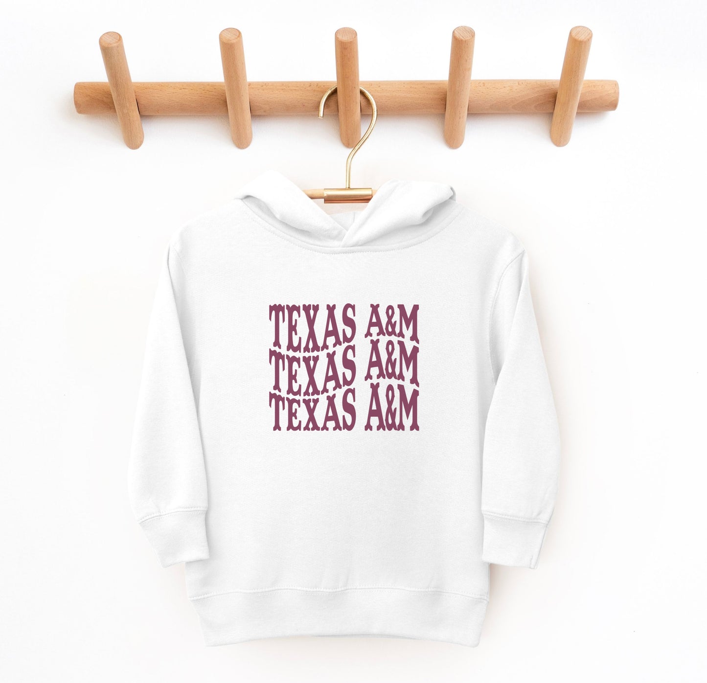 The White Toddler Unisex Texas A&M Western Hooded Sweatshirt lays flat on a white background. The ﻿Texas A&M Western﻿ graphic is in bold Maroon in a Western style.