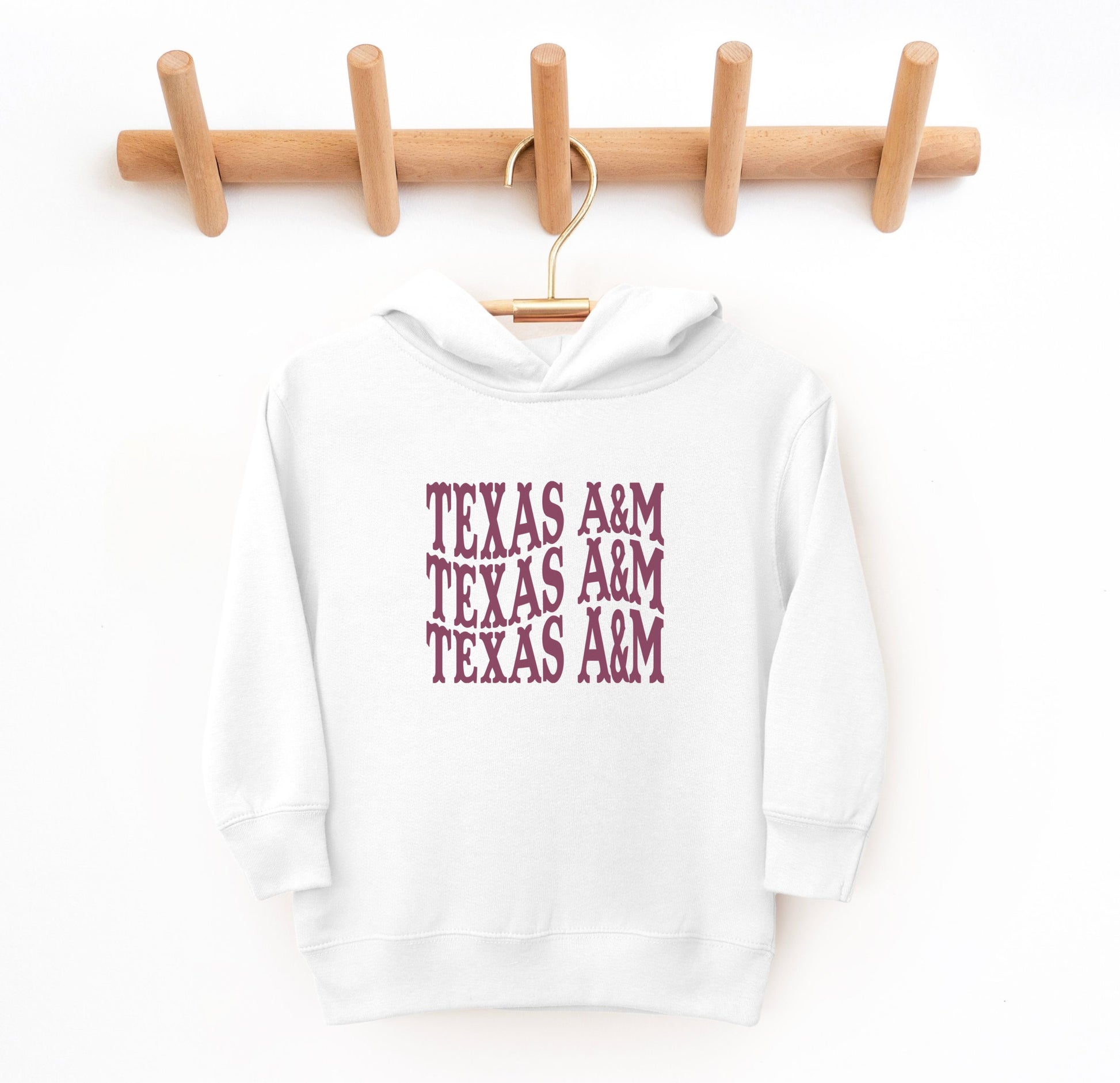 The White Toddler Unisex Texas A&M Western Hooded Sweatshirt lays flat on a white background. The ﻿Texas A&M Western﻿ graphic is in bold Maroon in a Western style.