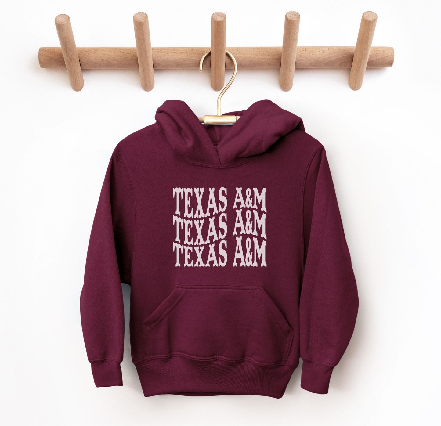 The Maroon Youth Unisex Texas A&M Western Hooded Sweatshirt lays flat on a white background. The ﻿Texas A&M Western﻿ graphic is in bold White in a Western style.