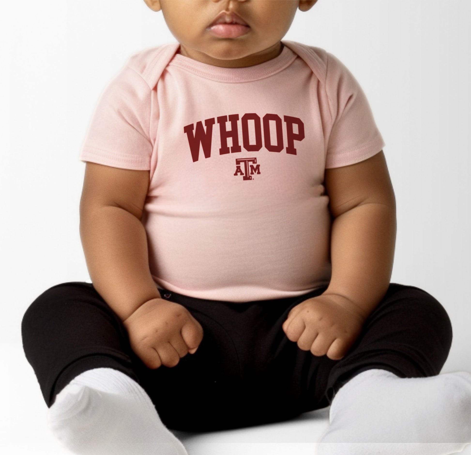 A model wears the Heather Grey Infant Unisex Texas A&M Whoop Collegiate Bodysuit.  The ﻿Texas A&M Whoop Collegiate﻿ graphic is in bold Maroon in a Varsity style.