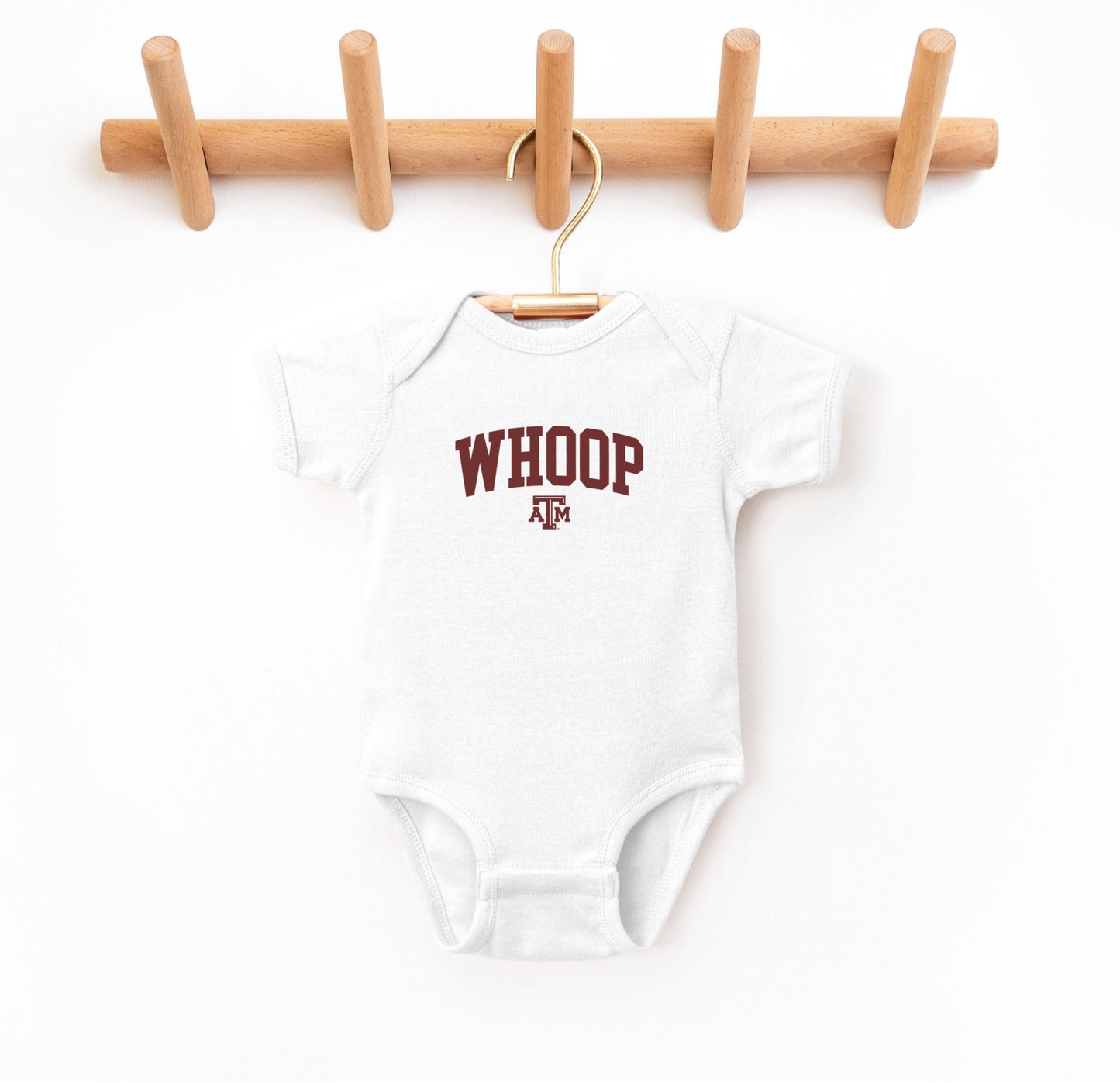 The White Infant Unisex Texas A&M Whoop Collegiate Bodysuit lays flat on a white background. The ﻿Texas A&M Whoop Collegiate﻿ graphic is in bold Maroon in a Varsity style.