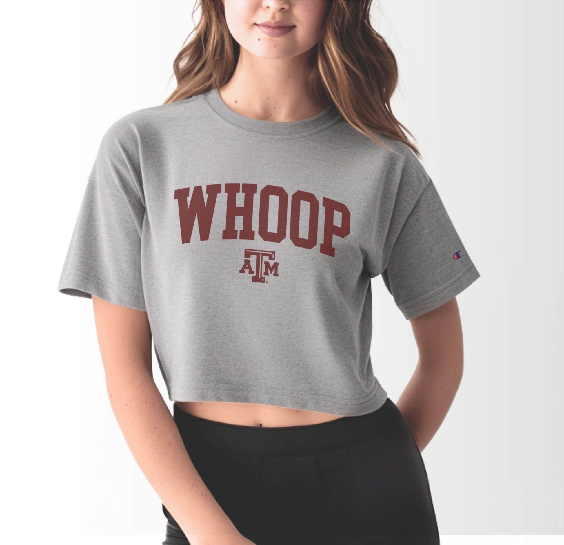 A model wears the Oxford Grey Adult Womens Texas A&M Whoop Collegiate Crop Top.  The ﻿Texas A&M Whoop Collegiate﻿ graphic is in bold Maroon in a Varsity style.