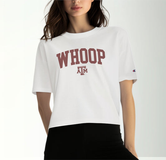 A model wears the White Adult Womens Texas A&M Whoop Collegiate Crop Top.  The ﻿Texas A&M Whoop Collegiate﻿ graphic is in bold Maroon in a Varsity style.