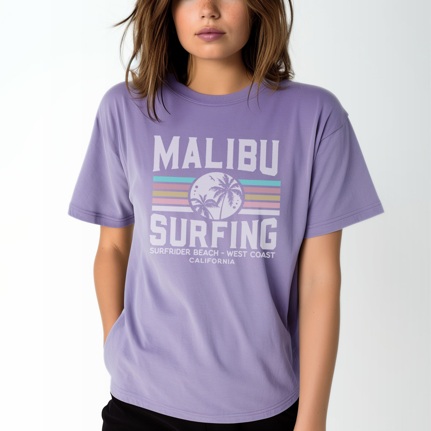 A model wears the Violet Adult Unisex Malibu California Surfing Comfort Colors T-shirt.  The ﻿Malibu California Surfing﻿ graphic is in bold Lifestyle in a Multicolor style.