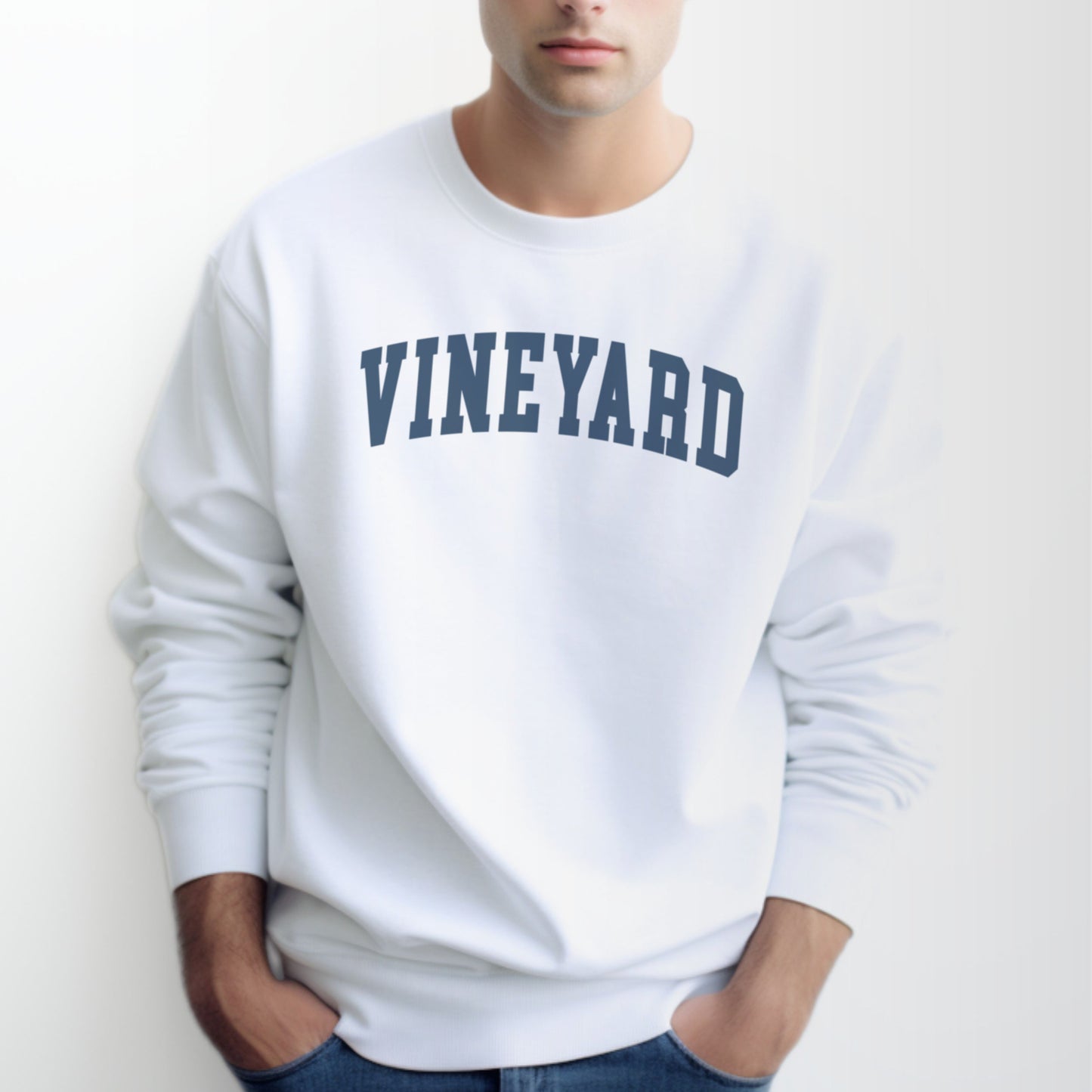 A model wears the White Adult Unisex Martha's Vineyard Massachusetts Classic Crewneck Sweatshirt.  The ﻿Martha's Vineyard Massachusetts Classic﻿ graphic is in bold Navy in a Varsity style.