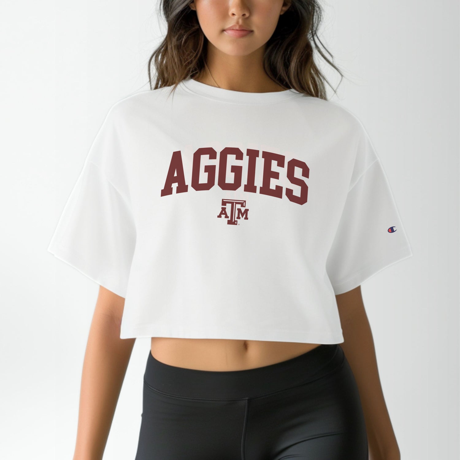 A model wears the White Adult Womens Texas A&M Aggies Collegiate Crop Top.  The ﻿Texas A&M Aggies Collegiate﻿ graphic is in bold Maroon in a Varsity style.