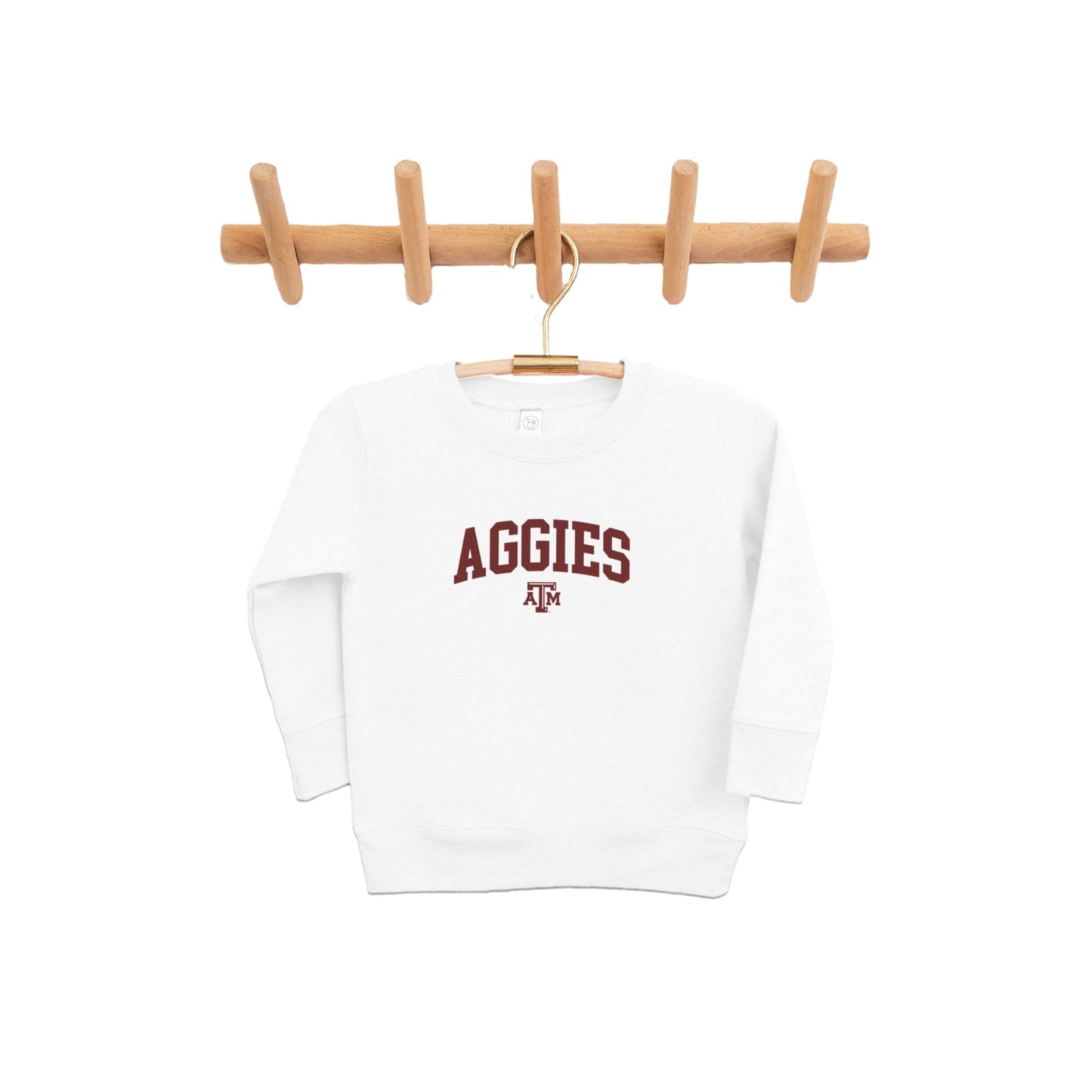 The white Toddler Texas A&M Aggies Collegiate Crewneck Sweatshirt hangs from a pine clothing rack.  The ﻿Texas A&M Aggies Collegiate﻿ graphic is in bold Maroon in a Varsity style.