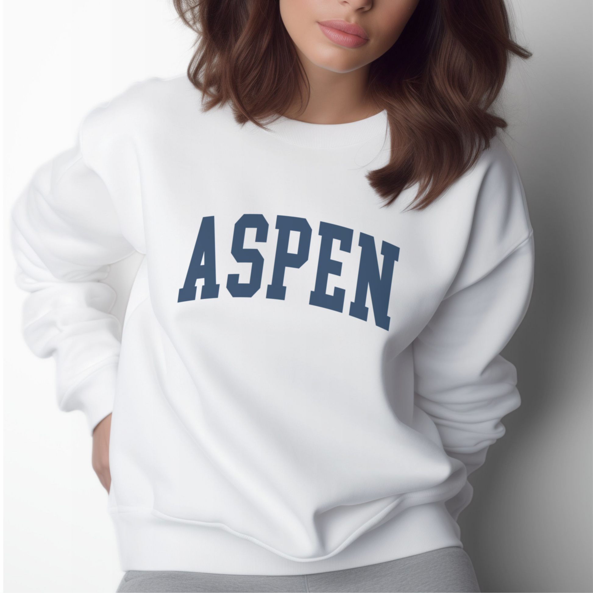 A model wears the White Aspen Colorado Varsity Crewneck Sweatshirt.  The ﻿Aspen Colorado Varsity﻿ graphic is in bold Navy in a Collegiate style.