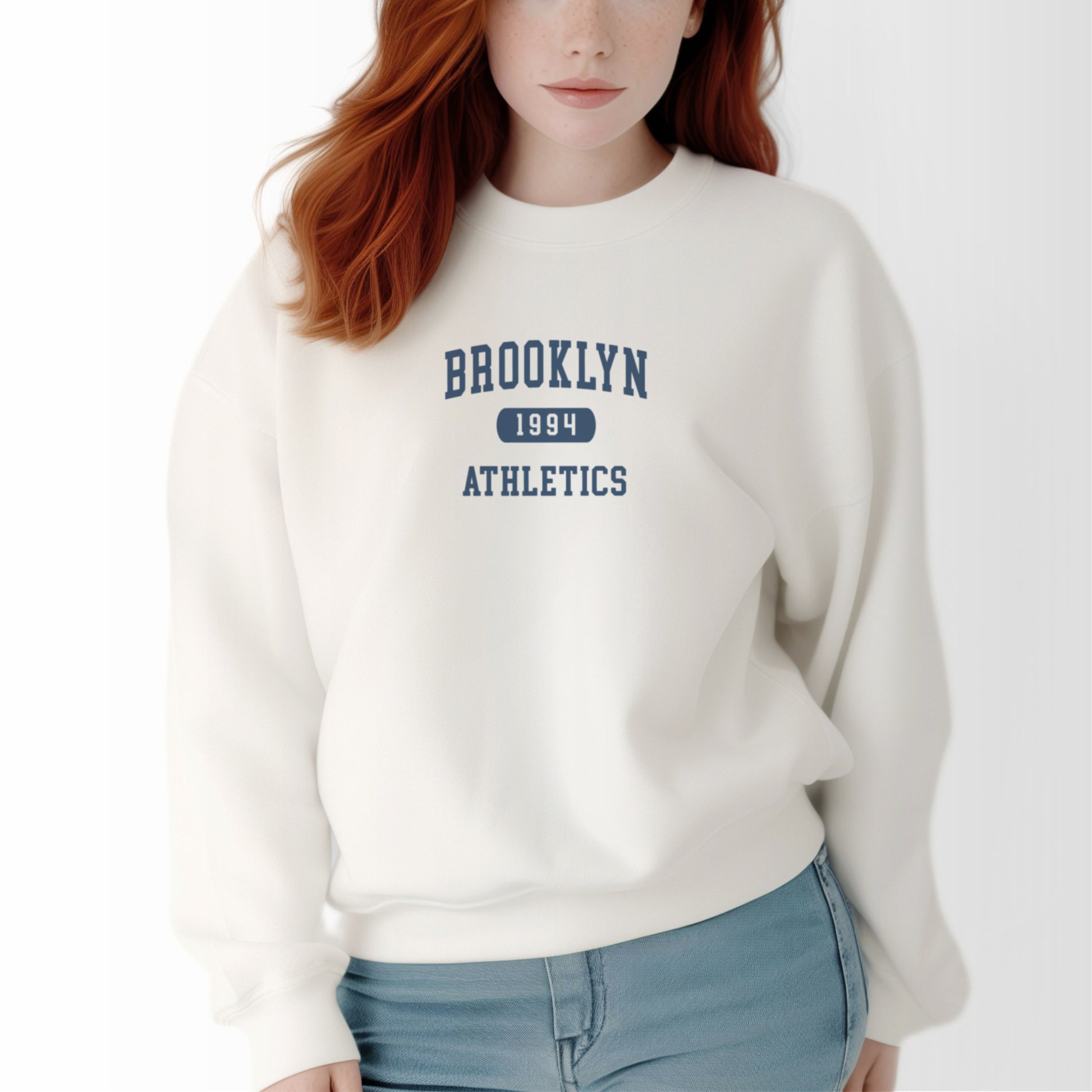 A model wears the White Brooklyn Athletics Crewneck Sweatshirt.  The ﻿Brooklyn Athletics﻿ graphic is in bold Navy in a Varsity style.