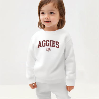 A young toddler wears the White Texas A&M Aggies Collegiate Crewneck Sweatshirt.  The ﻿Texas A&M Aggies Collegiate﻿ graphic is in bold Maroon in a Varsity style.